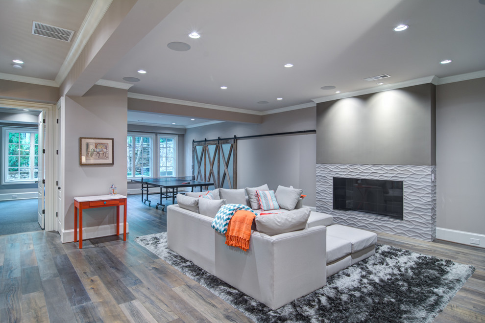 Cette image montre un grand sous-sol minimaliste donnant sur l'extérieur avec un mur gris, un sol en bois brun, une cheminée ribbon et un manteau de cheminée en carrelage.