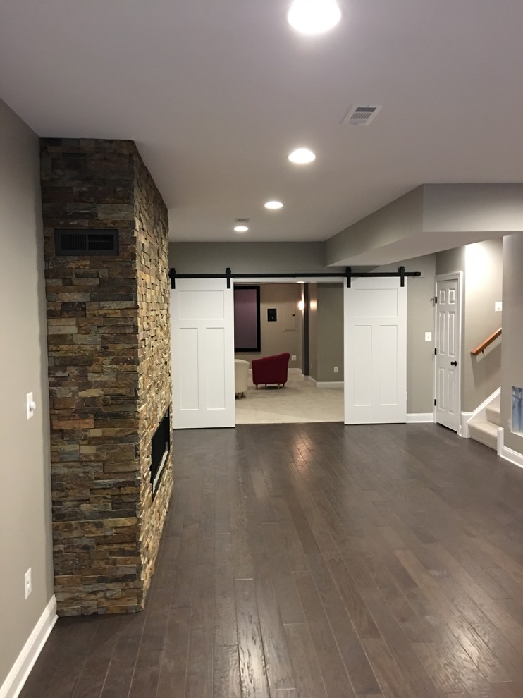 ワシントンD.C.にある広いコンテンポラリースタイルのおしゃれな地下室 (全地下、茶色い壁、濃色無垢フローリング、横長型暖炉、石材の暖炉まわり、茶色い床) の写真