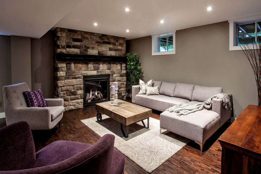 This is an example of a rustic look-out basement in Toronto with grey walls, dark hardwood flooring, a standard fireplace and a stone fireplace surround.