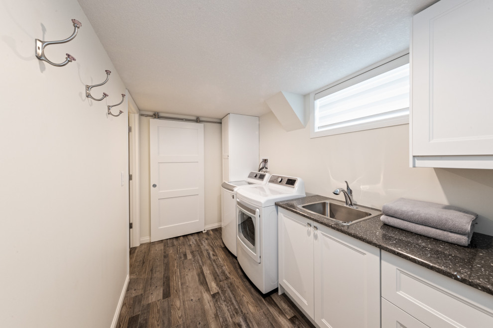 This is an example of a medium sized modern fully buried basement in Edmonton with a home bar, white walls, vinyl flooring, a standard fireplace, a tiled fireplace surround, brown floors and tongue and groove walls.