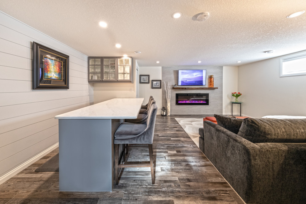 Cette image montre un sous-sol minimaliste enterré et de taille moyenne avec un bar de salon, un mur blanc, un sol en vinyl, une cheminée standard, un manteau de cheminée en carrelage, un sol marron et du lambris de bois.
