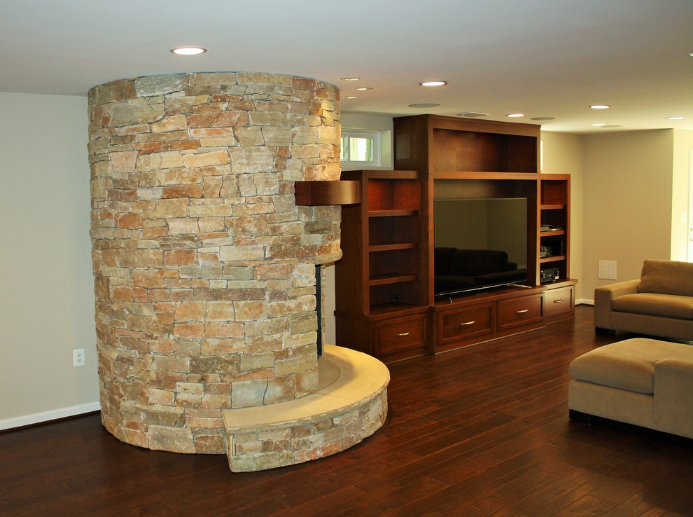Cette photo montre un grand sous-sol éclectique donnant sur l'extérieur avec un mur beige, parquet foncé, une cheminée standard et un manteau de cheminée en pierre.