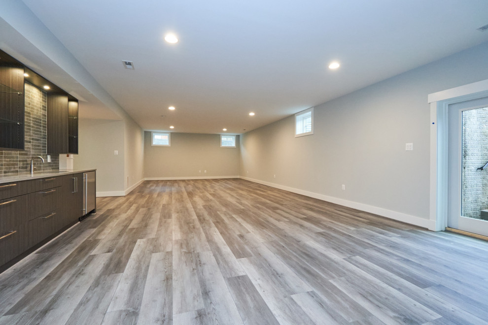 Aménagement d'un grand sous-sol classique donnant sur l'extérieur avec un mur gris, un sol en vinyl et un sol gris.