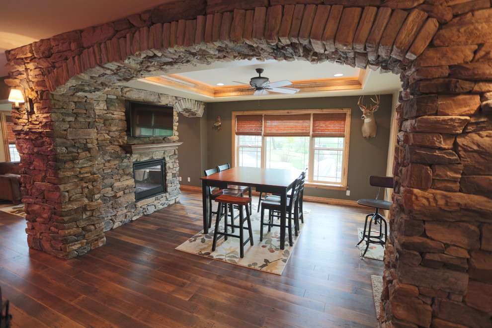 Mid-sized mountain style dark wood floor basement photo in Milwaukee with green walls, a two-sided fireplace and a stone fireplace