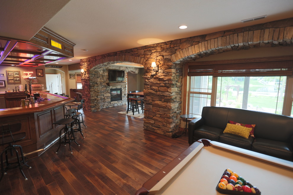 Large rustic basement in Milwaukee with beige walls, dark hardwood flooring, a two-sided fireplace and a stone fireplace surround.