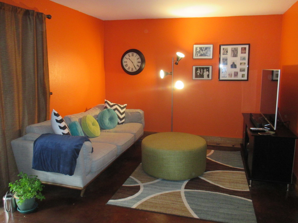 Exemple d'un petit sous-sol rétro donnant sur l'extérieur avec un mur orange, sol en béton ciré, un poêle à bois, un manteau de cheminée en pierre et un sol marron.