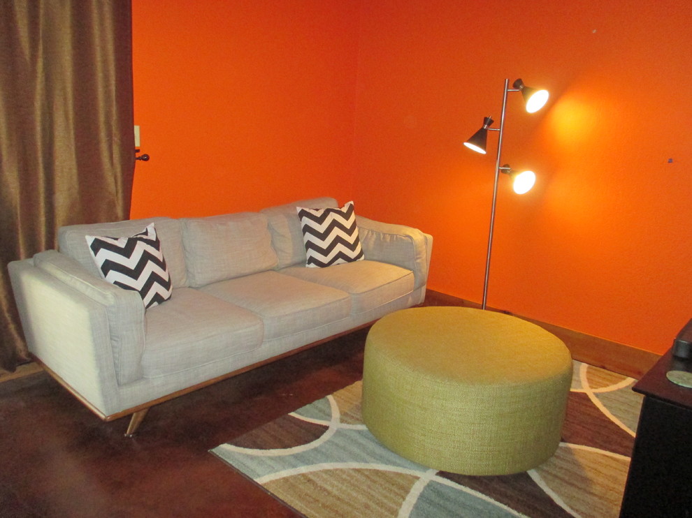 Immagine di una piccola taverna minimalista con sbocco, pareti arancioni, pavimento in cemento, stufa a legna, cornice del camino in pietra e pavimento marrone