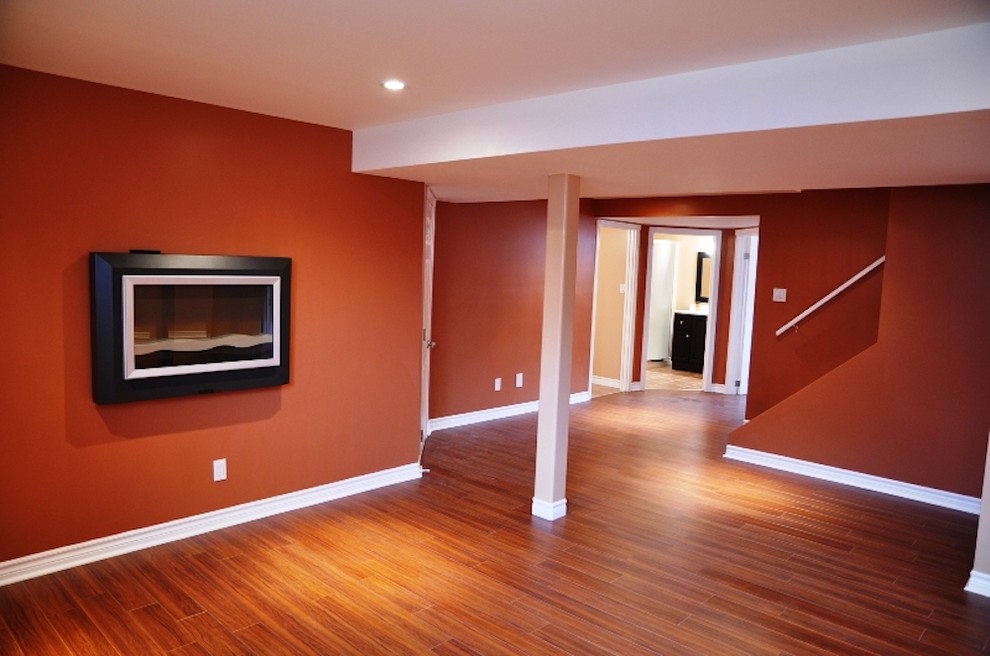 Cette image montre un sous-sol de taille moyenne avec un mur orange, un sol en bois brun, cheminée suspendue et un sol marron.