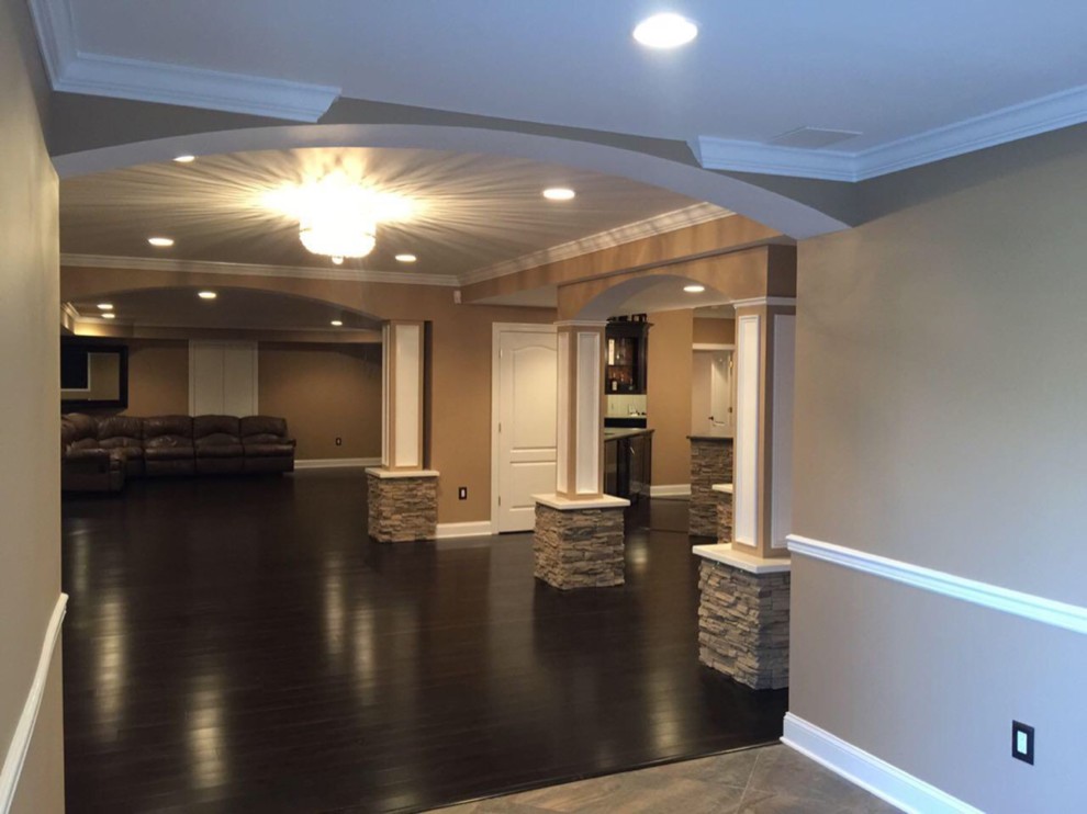 Medium sized traditional walk-out basement in New York with beige walls, bamboo flooring, a hanging fireplace, a stone fireplace surround and brown floors.