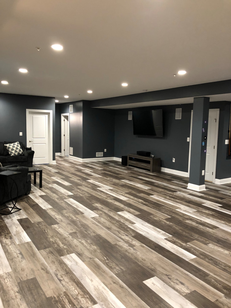 This is an example of a large modern look-out basement with black walls, vinyl flooring, no fireplace and brown floors.