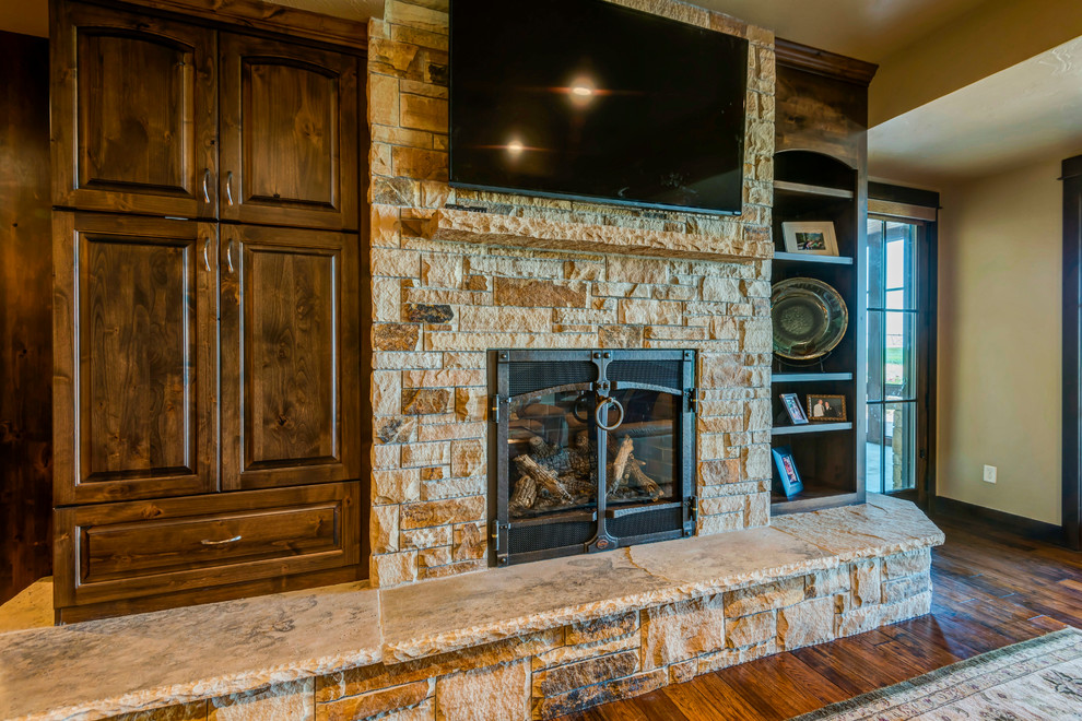 This is an example of a large classic walk-out basement in Denver with beige walls, medium hardwood flooring, a standard fireplace, a stone fireplace surround and brown floors.