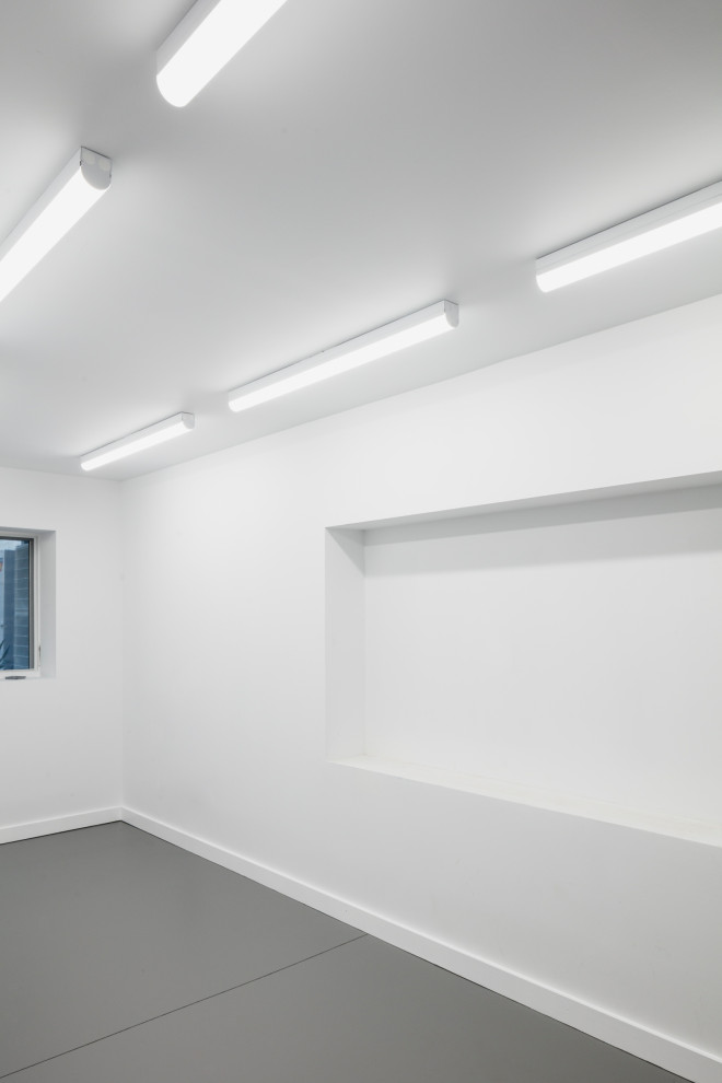 На фото: подвал в современном стиле с наружными окнами, белыми стенами и серым полом с