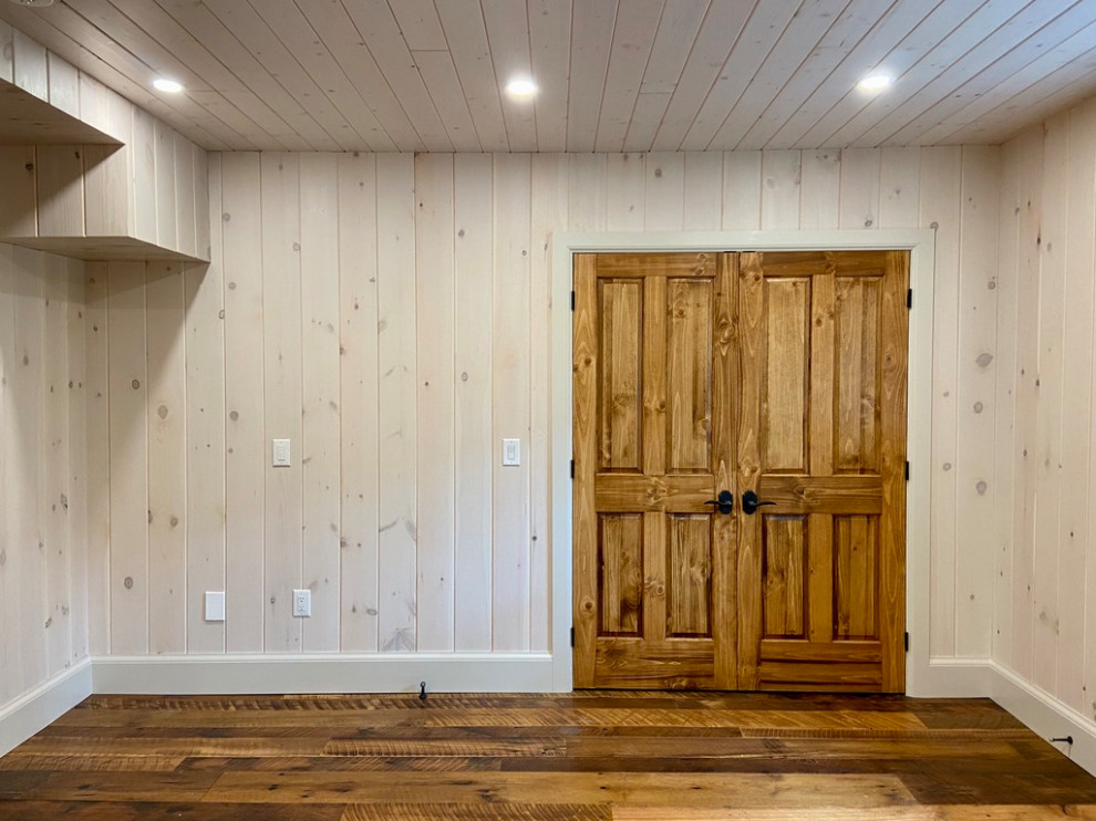 Exemple d'un sous-sol craftsman donnant sur l'extérieur et de taille moyenne avec salle de jeu, un mur blanc, un sol en bois brun, une cheminée standard, un manteau de cheminée en pierre, un sol marron, un plafond en lambris de bois et du lambris de bois.