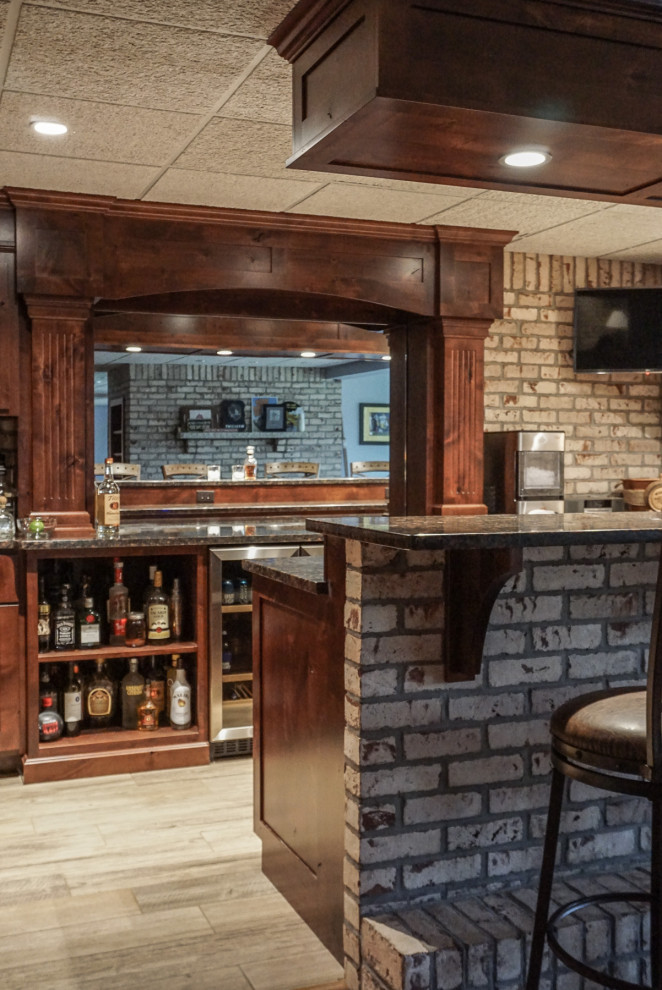 Small rustic walk-out basement in Other with a home bar, white walls, light hardwood flooring, a two-sided fireplace, a brick fireplace surround, grey floors and brick walls.