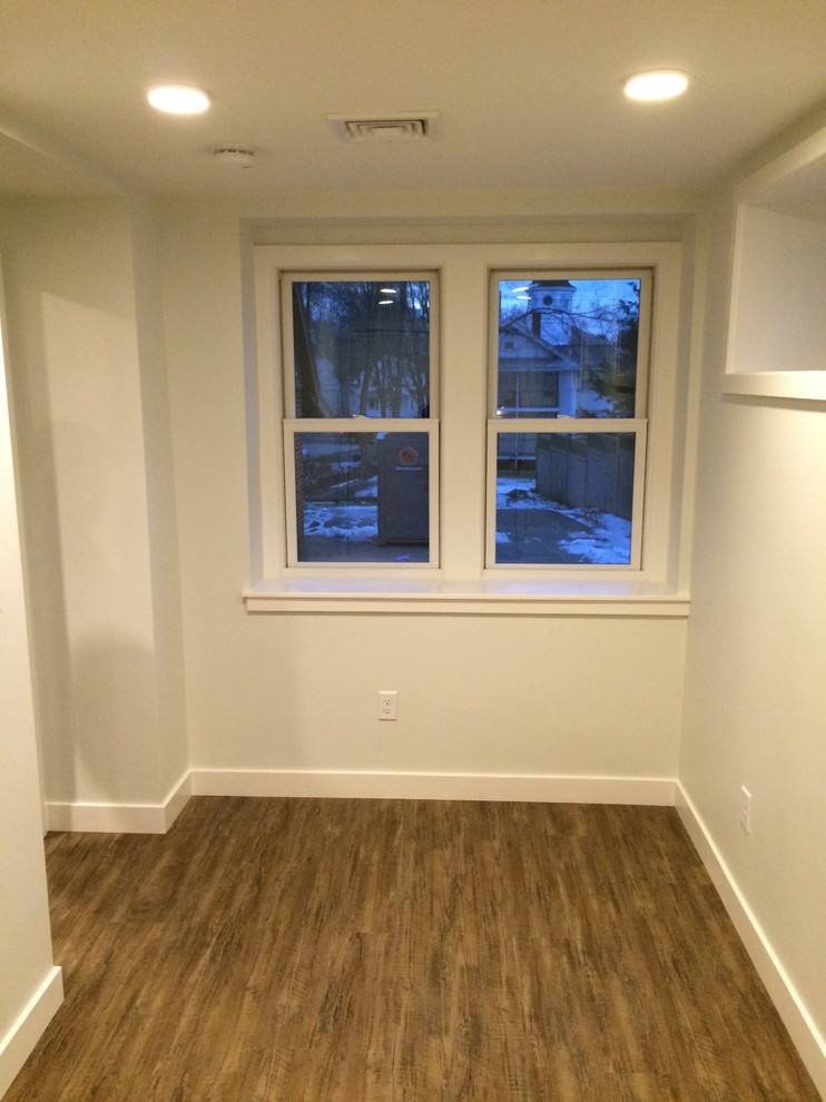 This is an example of a medium sized modern look-out basement in Boston with white walls, medium hardwood flooring, no fireplace and brown floors.