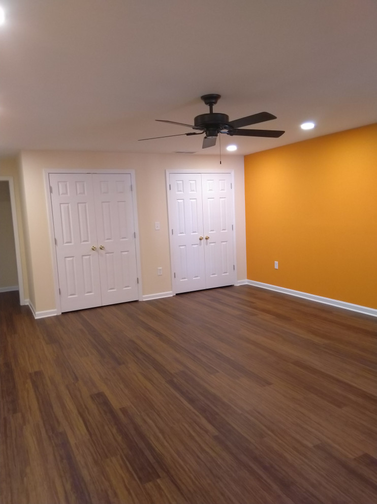 Cette image montre un grand sous-sol traditionnel avec un mur orange, un sol en vinyl, aucune cheminée et un sol marron.