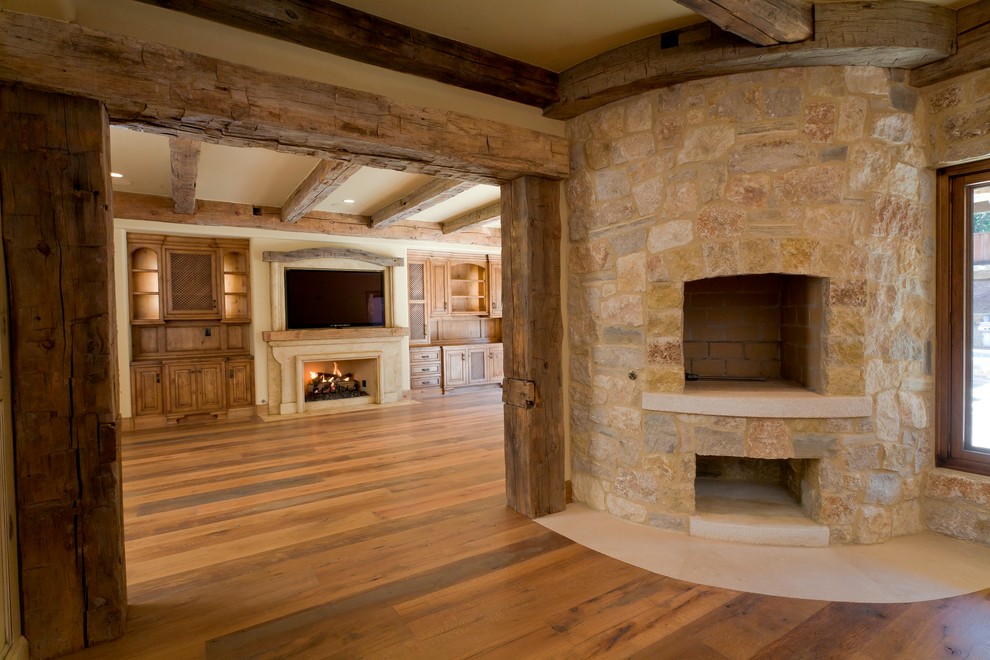 Idées déco pour un grand sous-sol classique avec un mur beige, un sol en bois brun, une cheminée d'angle et un manteau de cheminée en pierre.