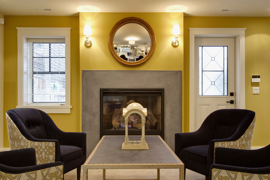 カルガリーにある高級な中くらいなトランジショナルスタイルのおしゃれな地下室 (半地下 (窓あり) 、黄色い壁、磁器タイルの床、標準型暖炉、コンクリートの暖炉まわり、ベージュの床) の写真