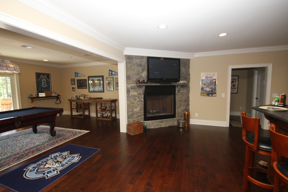 Example of a mid-sized classic walk-out dark wood floor and brown floor basement design in Raleigh with a standard fireplace, a stone fireplace and beige walls