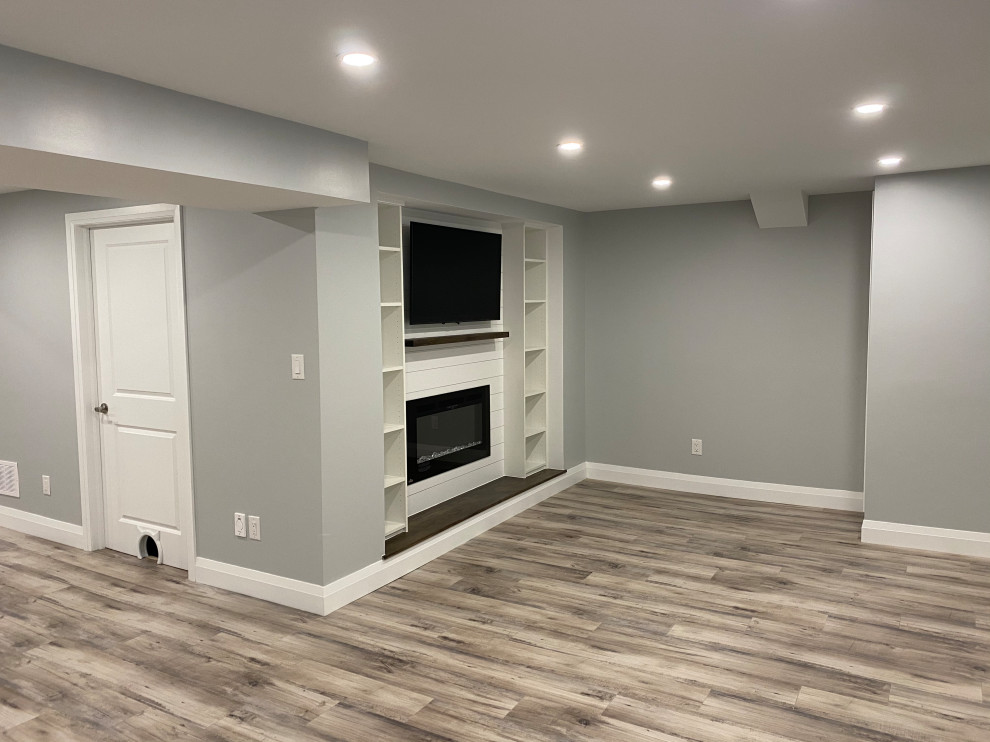 Kleines Modernes Untergeschoss mit grauer Wandfarbe, Laminat, Kamin, Kaminumrandung aus Holzdielen und braunem Boden in Toronto