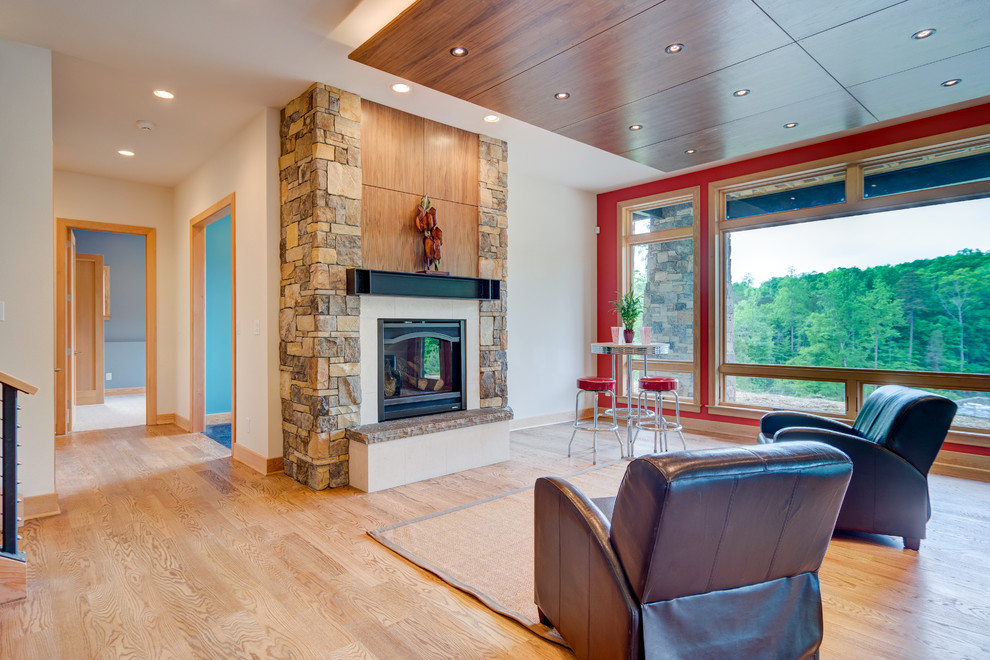 Idée de décoration pour un grand sous-sol minimaliste donnant sur l'extérieur avec un mur rouge, un sol en bois brun, une cheminée standard et un manteau de cheminée en pierre.