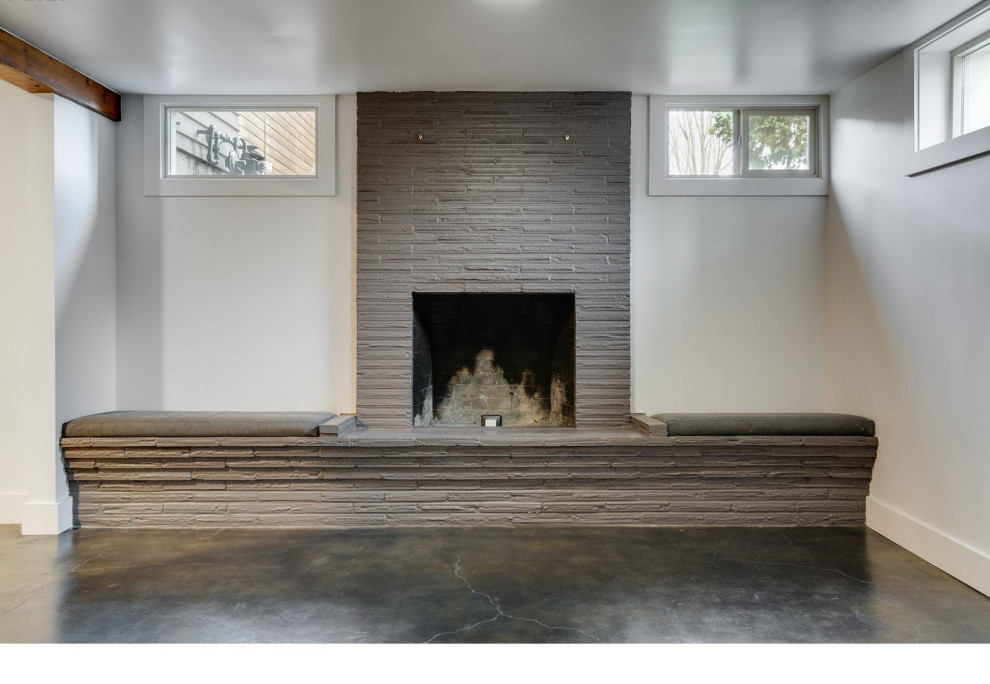 Cette photo montre un petit sous-sol craftsman semi-enterré avec un mur gris, sol en béton ciré, une cheminée standard, un manteau de cheminée en brique et un sol gris.