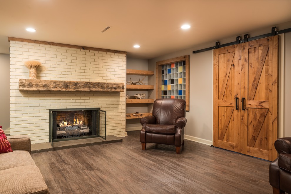 This is an example of a medium sized classic fully buried basement in Columbus with grey walls, vinyl flooring, a standard fireplace, a brick fireplace surround and brown floors.