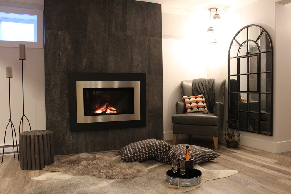 Réalisation d'un grand sous-sol minimaliste semi-enterré avec un mur gris, sol en stratifié, une cheminée standard, un manteau de cheminée en carrelage et un sol beige.