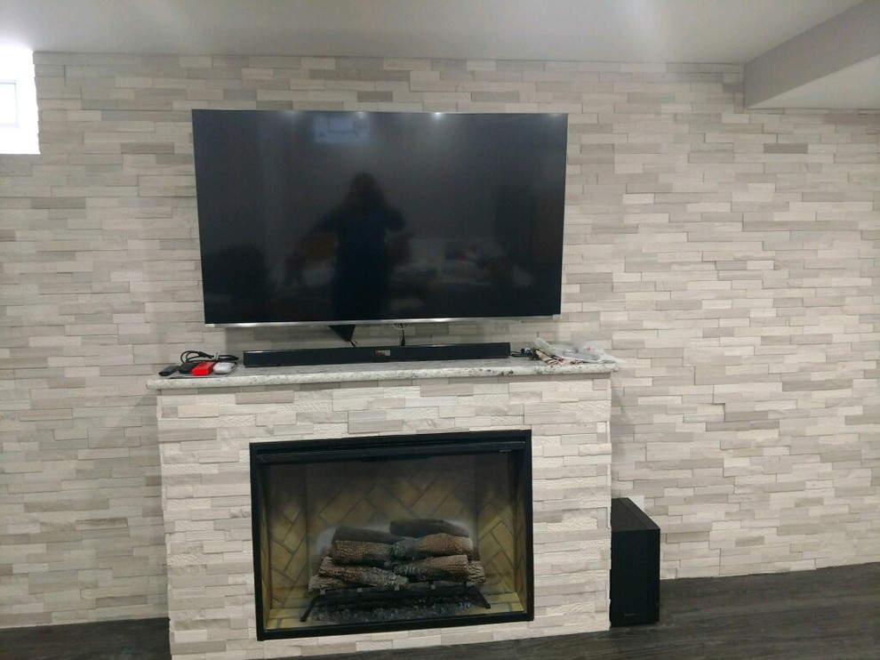 Example of a large eclectic underground medium tone wood floor and gray floor basement design in Chicago with gray walls, a standard fireplace and a stone fireplace
