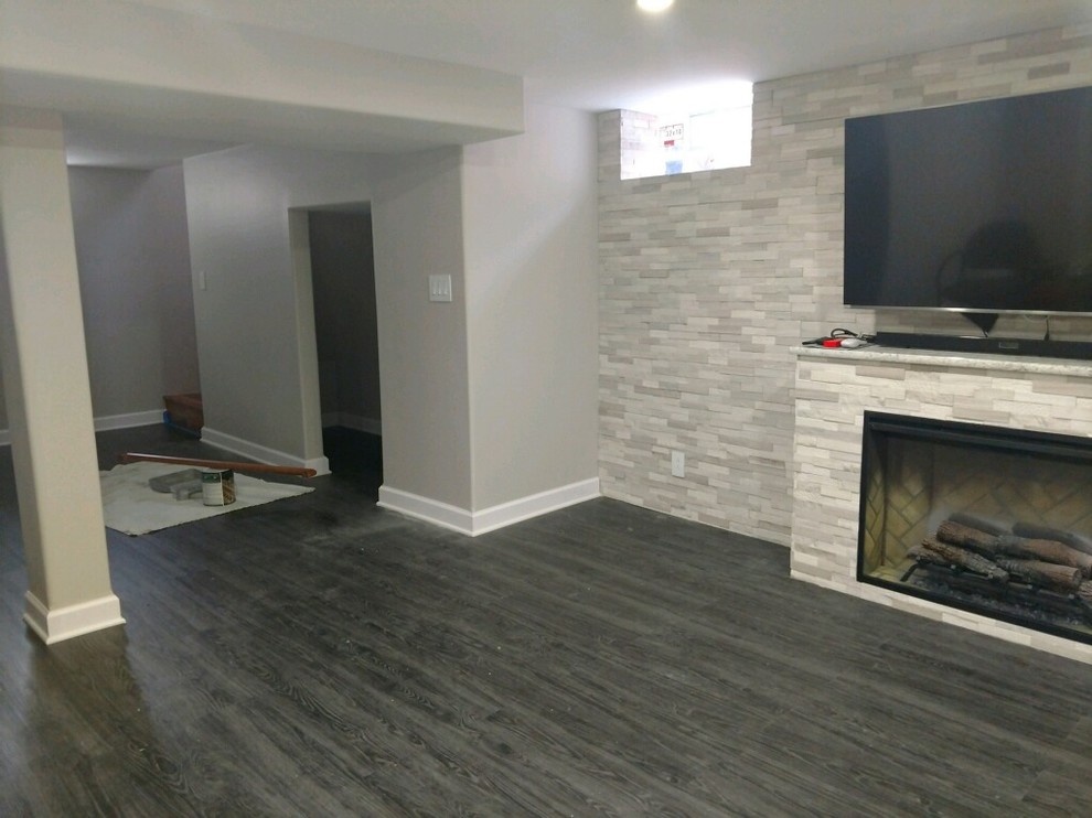 Design ideas for a large bohemian fully buried basement in Chicago with grey walls, medium hardwood flooring, a standard fireplace, a stone fireplace surround and grey floors.