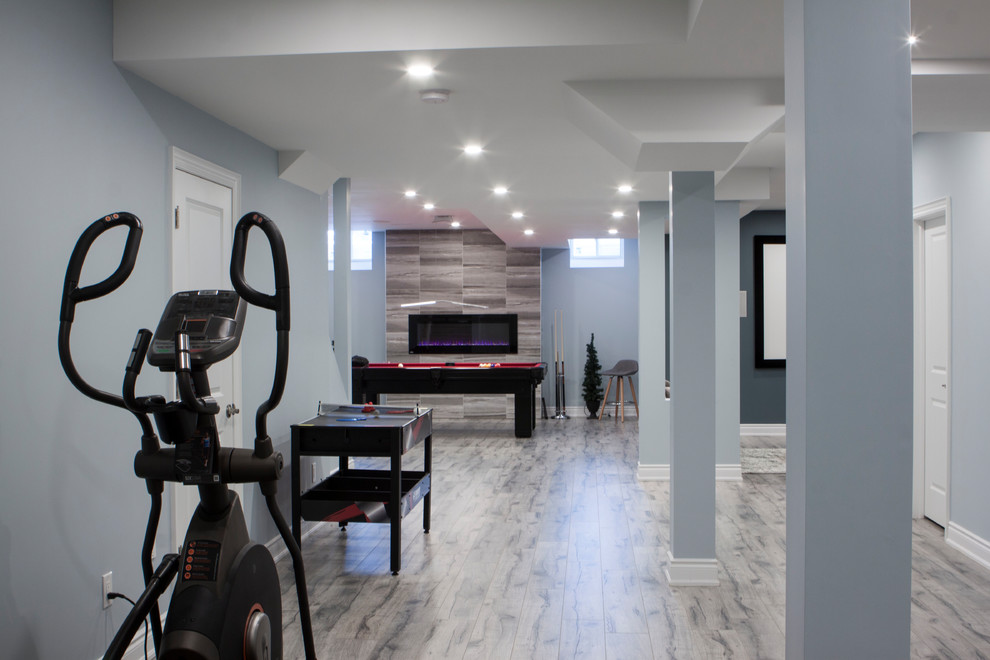 Inspiration for a large modern fully buried basement in Toronto with grey walls, laminate floors, a hanging fireplace, a tiled fireplace surround and grey floors.