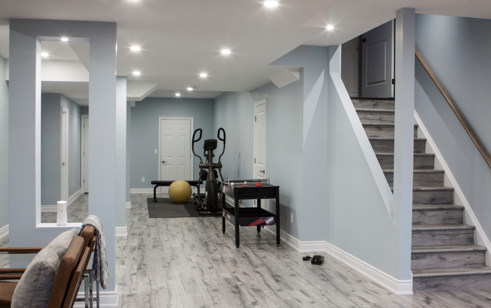 Inspiration for a large modern fully buried basement in Toronto with blue walls, laminate floors, a hanging fireplace, a tiled fireplace surround and grey floors.