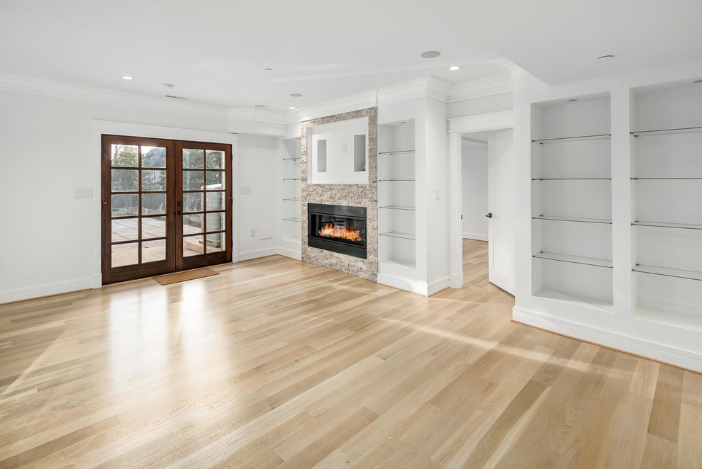 This is an example of a large modern walk-out basement in DC Metro with white walls, light hardwood flooring, a ribbon fireplace, a stone fireplace surround and beige floors.