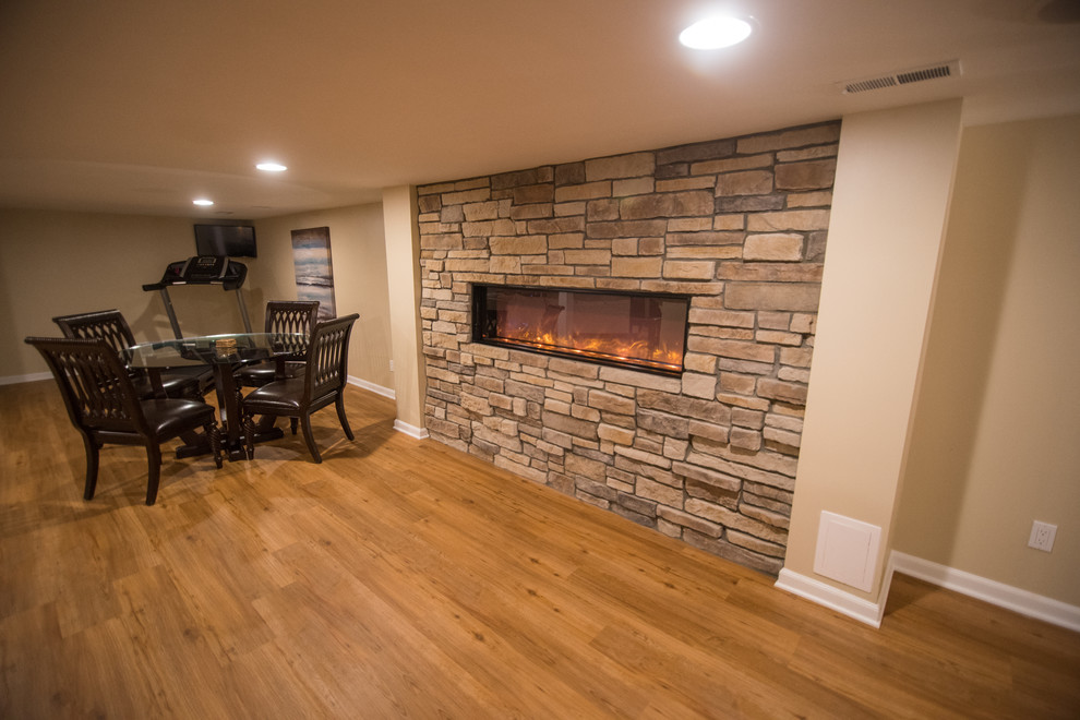 Aménagement d'un sous-sol classique avec un mur beige, un sol en vinyl, une cheminée standard et un manteau de cheminée en pierre.