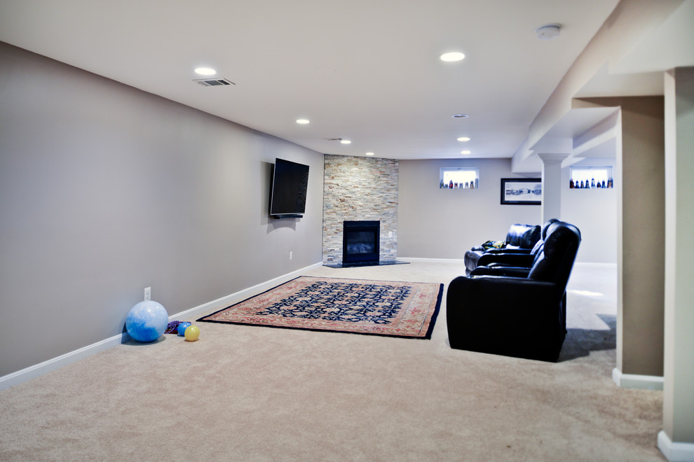 Cette photo montre un grand sous-sol chic avec un mur beige, moquette, une cheminée d'angle, un manteau de cheminée en pierre et un sol beige.