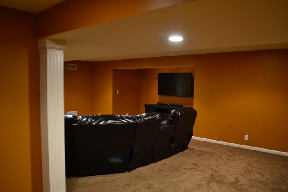 Aménagement d'un grand sous-sol classique enterré avec un mur orange, moquette, aucune cheminée et un sol marron.