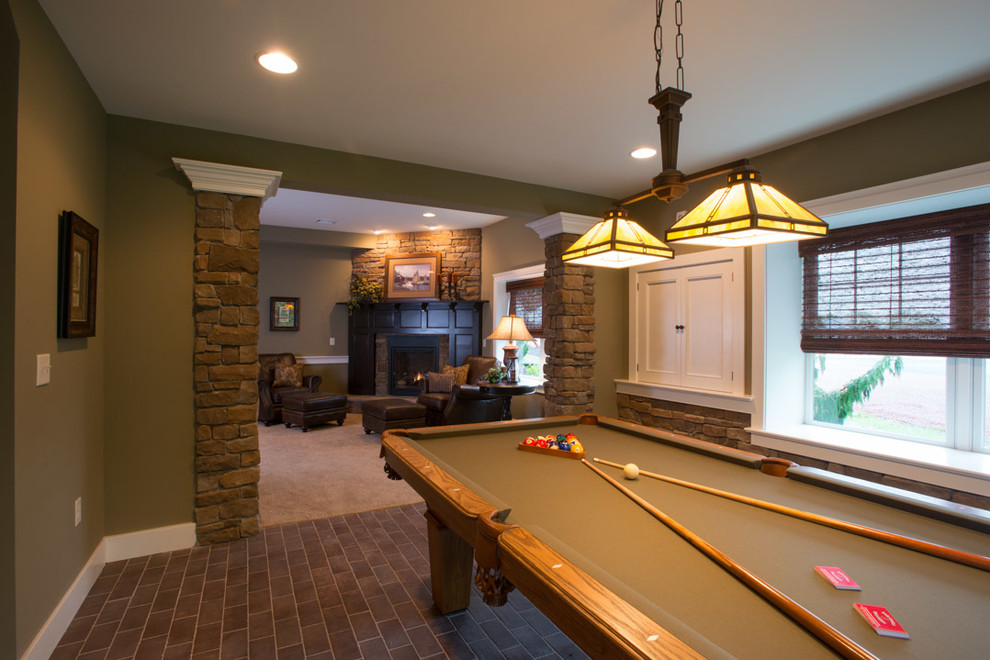 Exempel på en mycket stor amerikansk källare, med gröna väggar, tegelgolv, en standard öppen spis, en spiselkrans i sten och grått golv