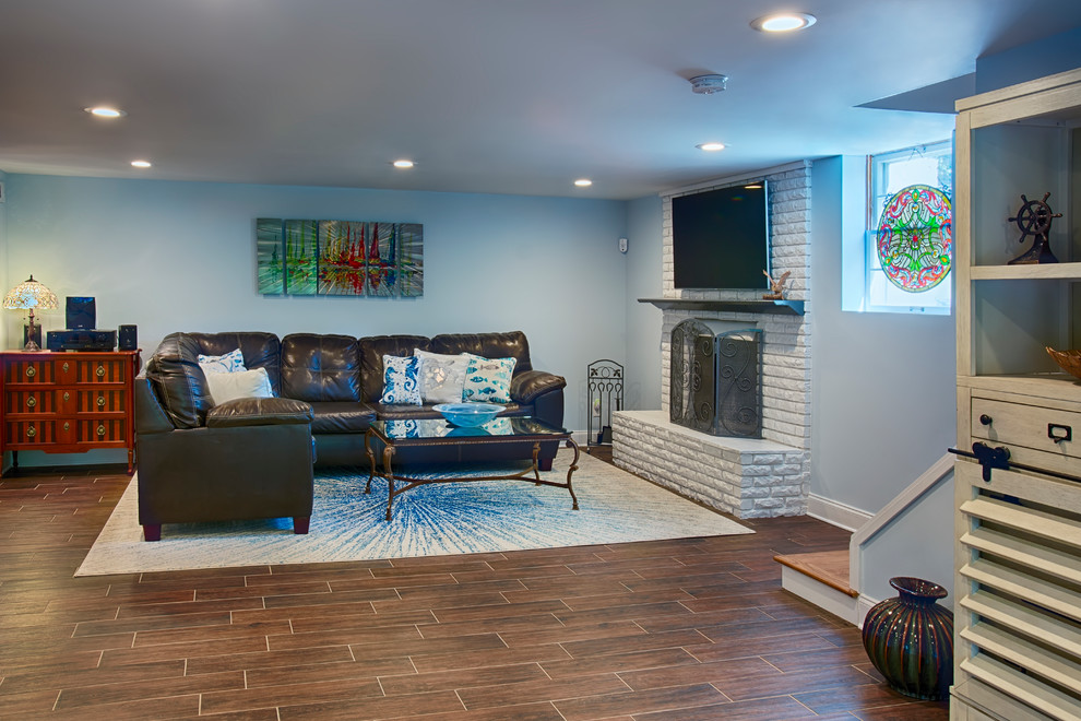 Idée de décoration pour un grand sous-sol design donnant sur l'extérieur avec un mur bleu, un sol en carrelage de céramique, une cheminée standard, un manteau de cheminée en pierre et un sol marron.