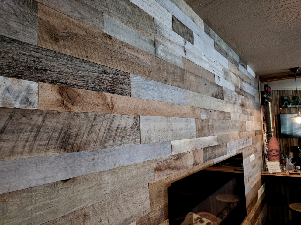 Example of a mountain style walk-out wood wall basement game room design in Other with gray walls, a hanging fireplace and a wood fireplace surround
