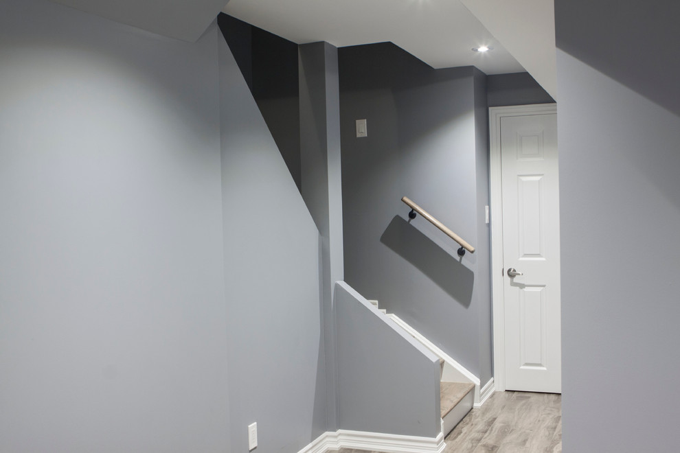 Inspiration pour un sous-sol minimaliste enterré et de taille moyenne avec un mur gris, une cheminée standard, un manteau de cheminée en pierre, sol en stratifié et un sol gris.