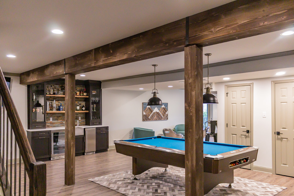 This is an example of a large rustic walk-out basement in Philadelphia with white walls, laminate floors, a corner fireplace, a stone fireplace surround and brown floors.