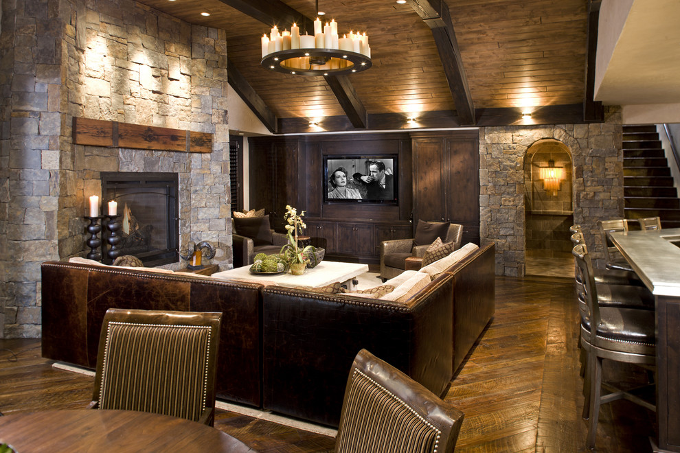 Пример оригинального дизайна: гостиная комната в стиле рустика с фасадом камина из камня, стандартным камином и темным паркетным полом
