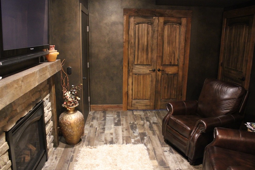 Aménagement d'un sous-sol craftsman de taille moyenne et enterré avec une cheminée standard, un manteau de cheminée en pierre, un mur noir, un sol en bois brun et un sol gris.
