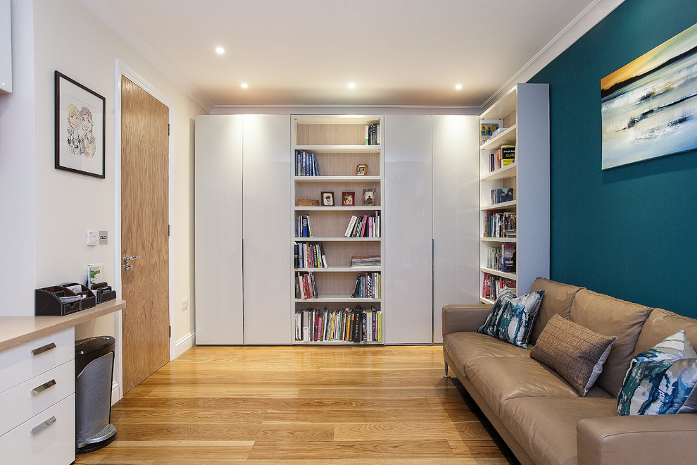 Photo of a large modern fully buried basement in London with white walls, light hardwood flooring and no fireplace.