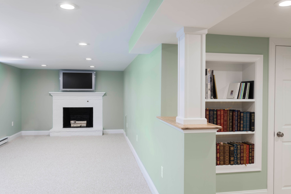 Cette photo montre un grand sous-sol chic avec un mur vert, moquette, une cheminée standard, un manteau de cheminée en brique et un sol gris.