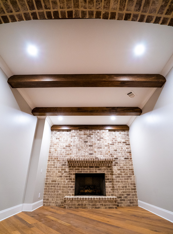 Idée de décoration pour un petit sous-sol champêtre enterré avec un bar de salon, un mur gris, un sol en bois brun, une cheminée standard, un manteau de cheminée en brique et un sol marron.