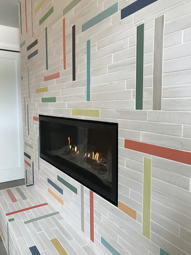 Cette photo montre un petit sous-sol moderne avec un mur multicolore, un sol en carrelage de porcelaine, une cheminée standard, un manteau de cheminée en carrelage et un sol gris.