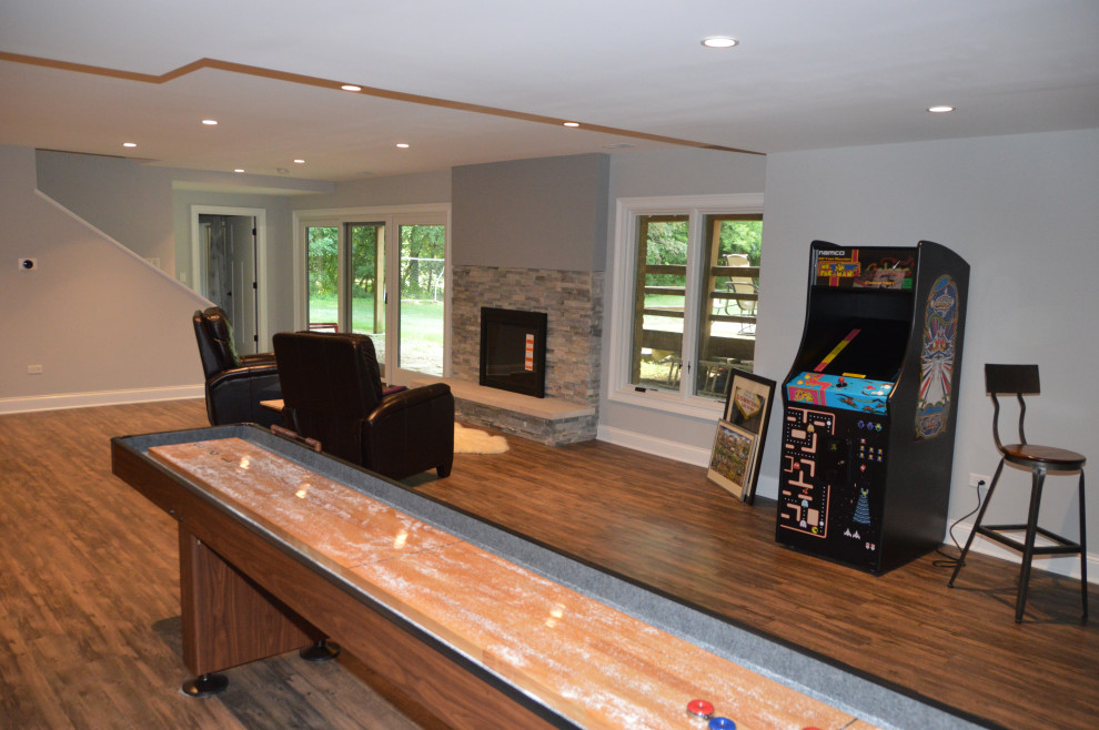 Inspiration for a medium sized traditional walk-out basement in Chicago with grey walls, medium hardwood flooring, a standard fireplace, a stone fireplace surround and brown floors.