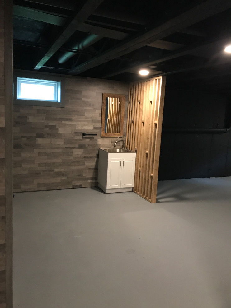 Immagine di una taverna minimalista interrata di medie dimensioni con pareti nere, pavimento in cemento, pavimento grigio e travi a vista