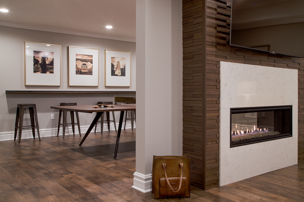 Transitional underground vinyl floor and brown floor basement photo in Detroit with gray walls, a two-sided fireplace and a wood fireplace surround